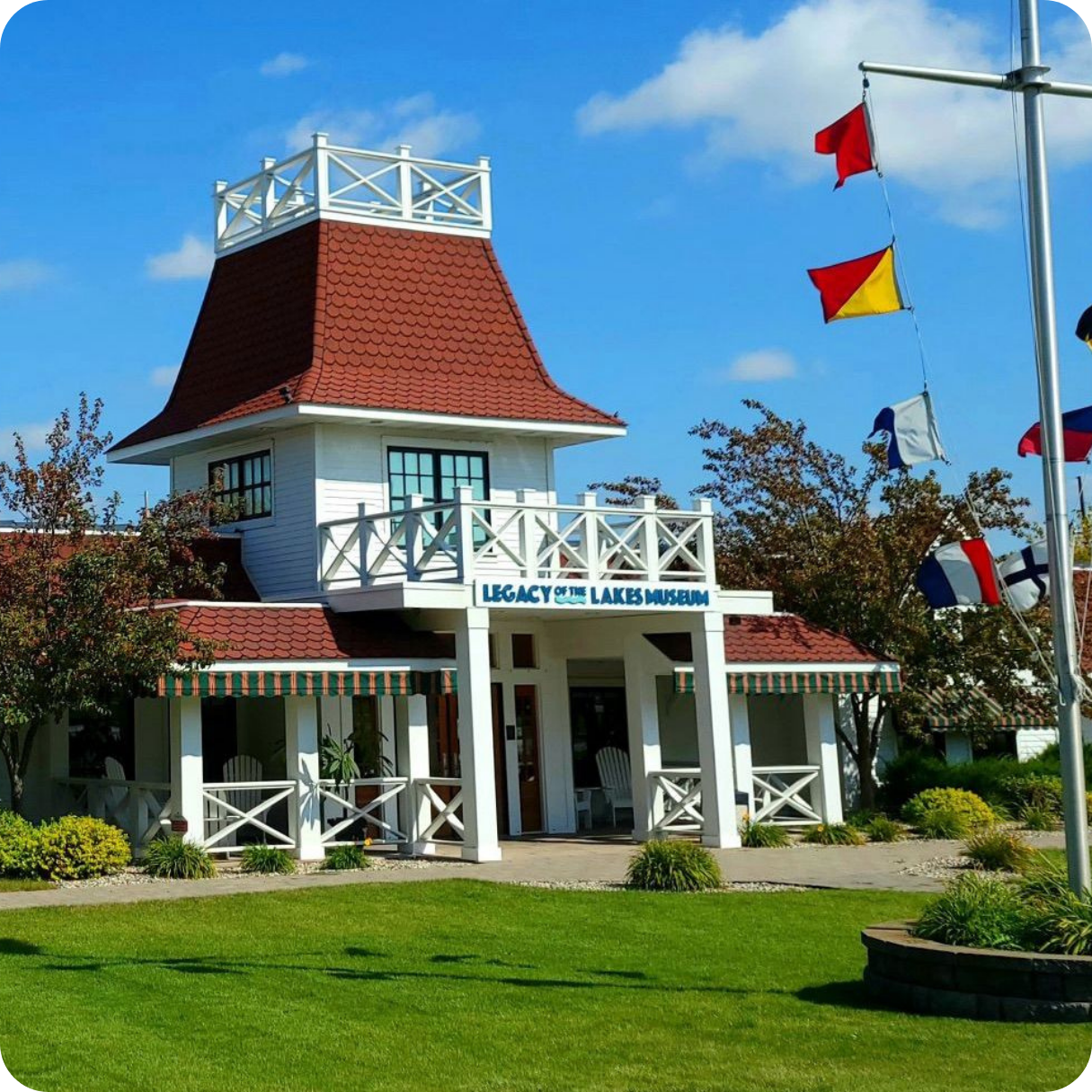 A withe and red building with a bright green lawn against a blue sky. The Sign on the front says 